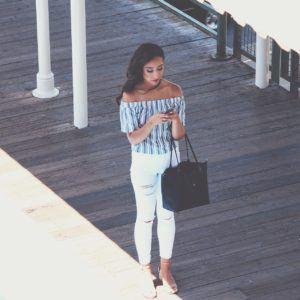 Dziewczyna smsująca do swojego chłopaka ubrana w białe spodnie z czarną torebką